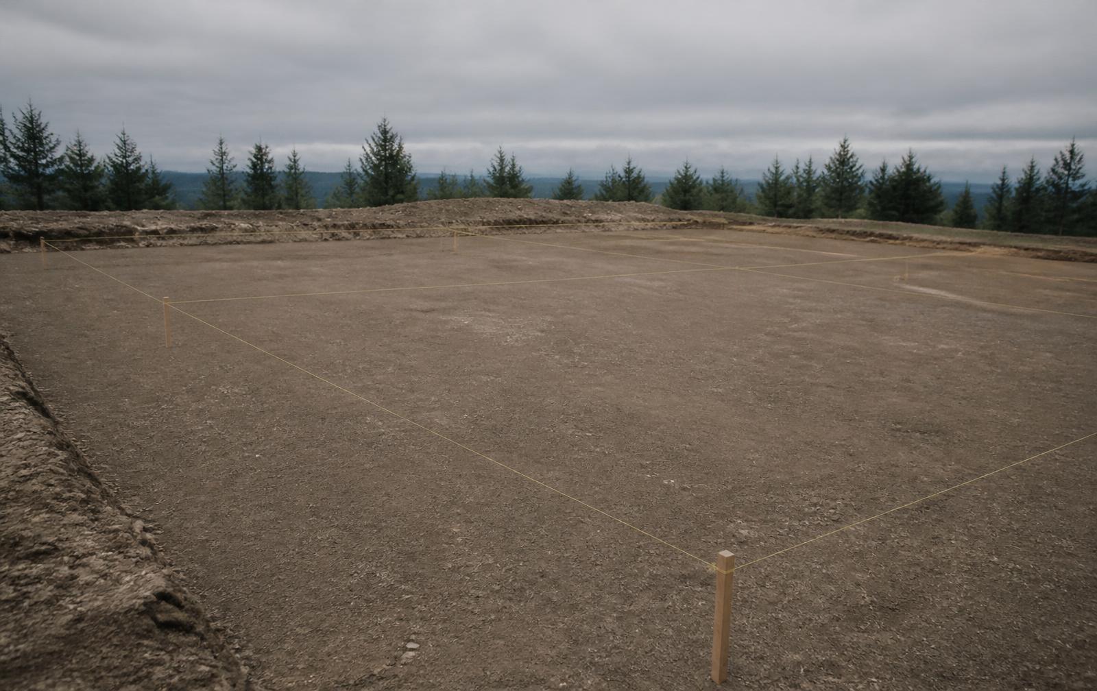 Laser-trimmed final building pad with taut yellow string lines marking footing positions, overcast light